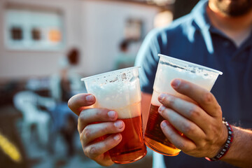 Person holding beer cup outdoors on a sunny day.