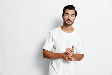 Full body thoughtful smiling young man wearing a white t-shirt looking at the camera, standing with...