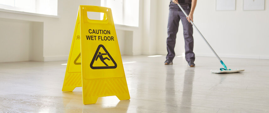 Yellow Caution Wet Floor sign warning of hazardous surface, person mopping floor indoor performing cleaning task and ensuring safety, maintenance and hazard awareness, professional cleaning service