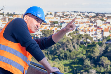 Building contractor wearing protective helmet and safety reflective jacket pointing upwards