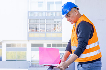 Absorbed construction engineer or building contractor wearing a blue protective helmet checking office blueprints. Copy space