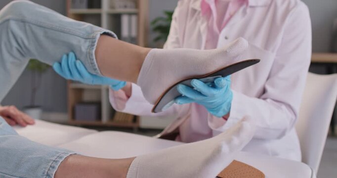 Orthopedist showing orthopedic insole to female patient lying on couch in medical clinic. Doctor consulting woman about feet health standing in office. Medicine and orthopedics concept. 4k video