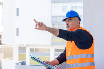Building contractor wearing protective helmet and safety reflective jacket pointing forwards