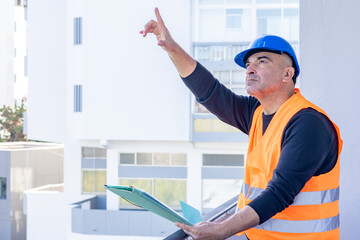 Building contractor wearing protective helmet and safety reflective jacket pointing upwards