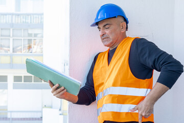 Fototapeta premium Injured construction worker or engineer suffering backpain. A warehouse worker in pain holding his back and making painful grimace