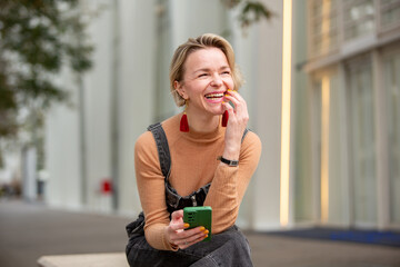 cheerful woman sitting outdoors in the city holding her phone ion hand