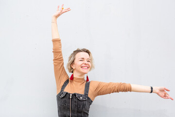 Smiling blond woman in stretch pose with arms raised against white wall