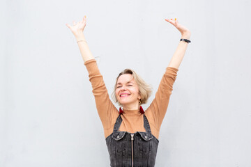 Blond woman full of confidence posing against white wall with arms raised