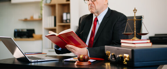 Senior Caucasian lawyer at office desk working on laptop with gavel and legal book. Justice, law,...