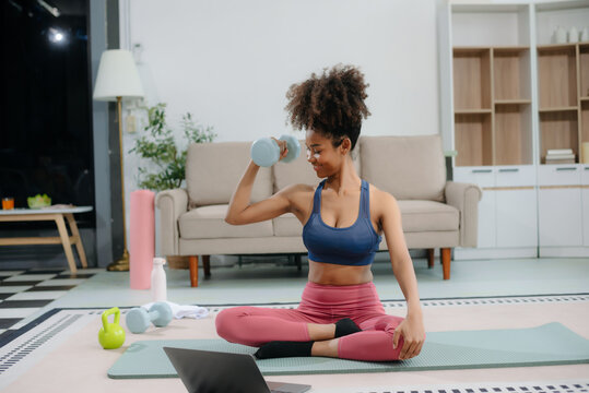 woman exercising at home on yoga mat, stretching, lifting dumbbells, and staying fit with energy, strength, and a healthy lifestyle.