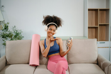 A sporty woman in sportswear sits with dumbbells, a protein shake, and a laptop. Fitness, recreation