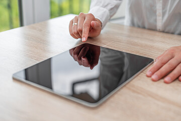 A person in a white shirt interacts with a tablet on a white table.