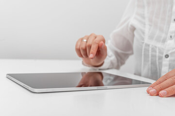 A person in a white shirt interacts with a tablet on a white table.