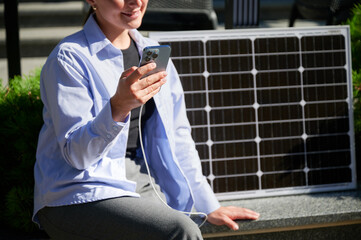 Happy woman using smartphone connected to solar panel. Cropped view. Integration of sustainable...