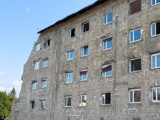 Weathered apartment building with exposed brick and broken windows under blue sky
