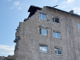 Partially collapsed building with exposed interior and damaged roof on cloudy day
