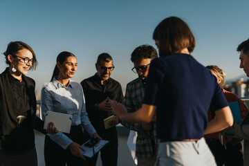 A diverse group of business people relax and socialize on a high-rise balcony at sunset, enjoying...