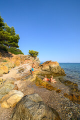 Little boys playing, laughing, and swimming among rocks in the sea on a wild beach. Joyful summer moment full of energy, freedom, and childhood adventure in nature.