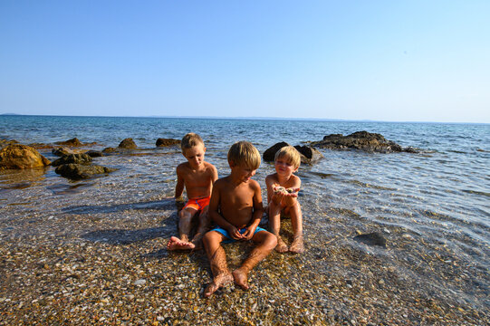 Little boys playing, laughing, and swimming among rocks in the sea on a wild beach. Joyful summer moment full of energy, freedom, and childhood adventure in nature. - Powered by Adobe