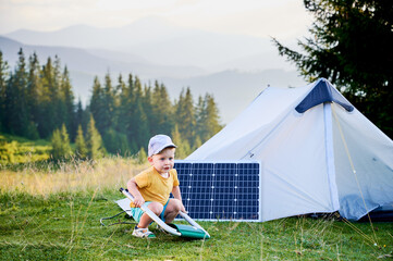 Young child playing near tourist tent with photovoltaic solar panel in summer. On background of...