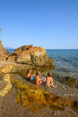Little boys playing, laughing, and swimming among rocks in the sea on a wild beach. Joyful summer moment full of energy, freedom, and childhood adventure in nature.