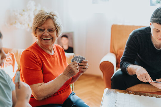 An elderly woman sharing a joyful moment playing cards with loved ones in a warm, inviting home setting filled with laughter and togetherness.