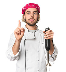 Young Caucasian chef using mixer in studio showing number one with finger.