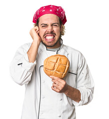 Young chef with artisan bread in studio covering ears with hands.