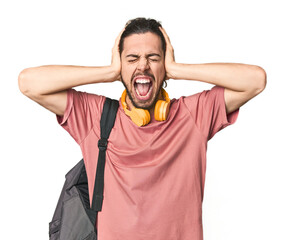 Young student with backpack and headphones covering ears with hands trying not to hear too loud...