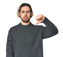 Young Caucasian man in studio setting showing a dislike gesture, thumbs down. Disagreement concept.