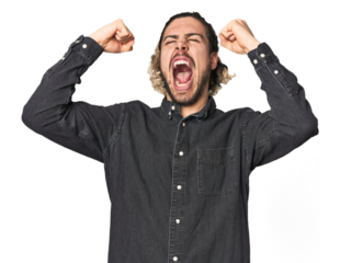 Young Caucasian man in studio setting raising fist after a victory, winner concept.