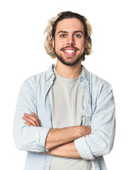 Young Caucasian man in studio setting who feels confident, crossing arms with determination.