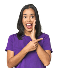 Young Latina posing in studio saying a gossip, pointing to side reporting something.