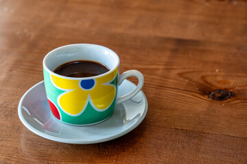 Colorful vintage coffee cup on a wooden table, a still life with a retro and happy mood. Cheerful and vibrant mug for a morning break. Positive start to the day with a hot drink like espresso