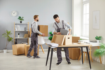 Moving office, two men in overalls packing boxes, carrying items, placing belongings on desk,...