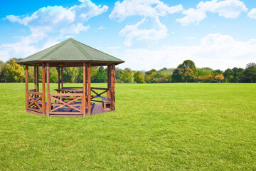 Wooden gazebos with picnic table and wooden bench in a green mowed lawn
