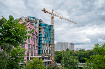 Construction crane against the backdrop of urban development, high-rise buildings and trees