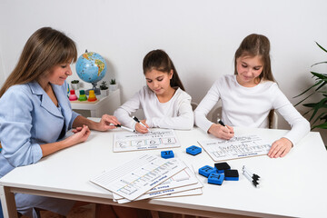 A cheerful scene of a teacher assisting two young girls learning math with marker boards for...