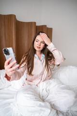 Young woman taking selfie in bedroom while sitting on bed during relaxed morning hours