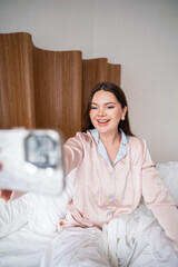 Joyful woman holding smartphone while sitting in bed