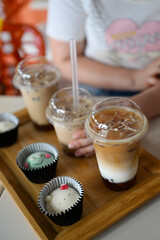 Iced Bubble Tea and Cute Mochi Desserts on Wooden Tray with a young girl's hand holding a bubble teacup in the background