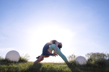 Two athletic individuals performing a dynamic yoga pose outdoors, surrounded by green grass and...