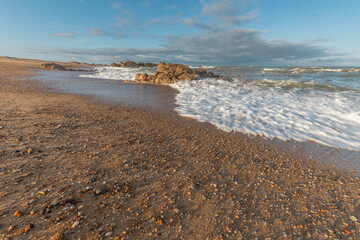 Serene sandy beach with pebbles and crashing waves at sunset in a coastal location