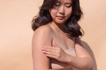Asian woman applying skincare product to her shoulder, showcasing a radiant glow, with soft...