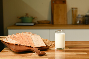 A glass of milk sits on a wooden table next to a tray of bread. The scene is simple and...