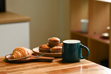 A plate of muffins and a cup of coffee sit on a wooden table. The muffins are arranged in a basket, and the coffee is in a mug.