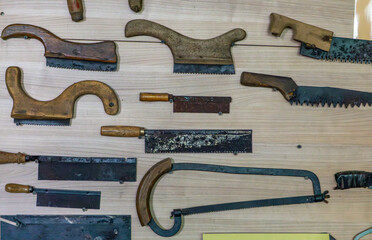 Vintage hand saws and carpentry tools arranged on a wooden surface. Various handle shapes and...