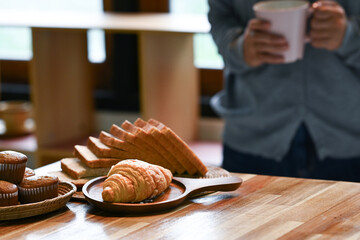 A person is holding a cup of coffee and a plate of croissants. The croissants are arranged on a...