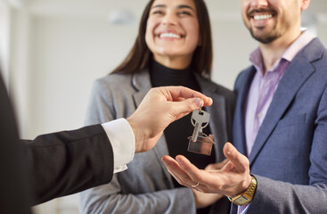 Closeup of professional male realtor giving house key to a young happy smiling couple customers....