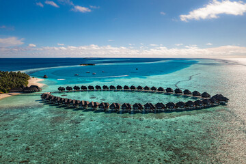 Stunning summer aerial landscape Maldives water villas pristine sea lagoon, sunny blue sky clouds perfect island shore. Beautiful palm trees tropical paradise vacation tourism luxury resort escape